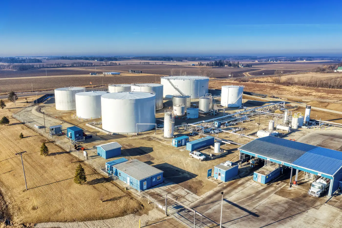 Aerial view of a small cluster of white crude storage tanks surrounded by flat farmland.
